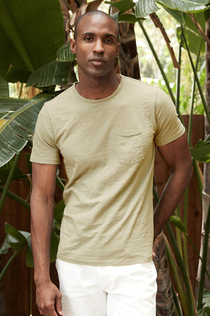 Chad Raw Edge Cotton Slub Pocket Tee in Olivine with white denim model standing outside near plants
