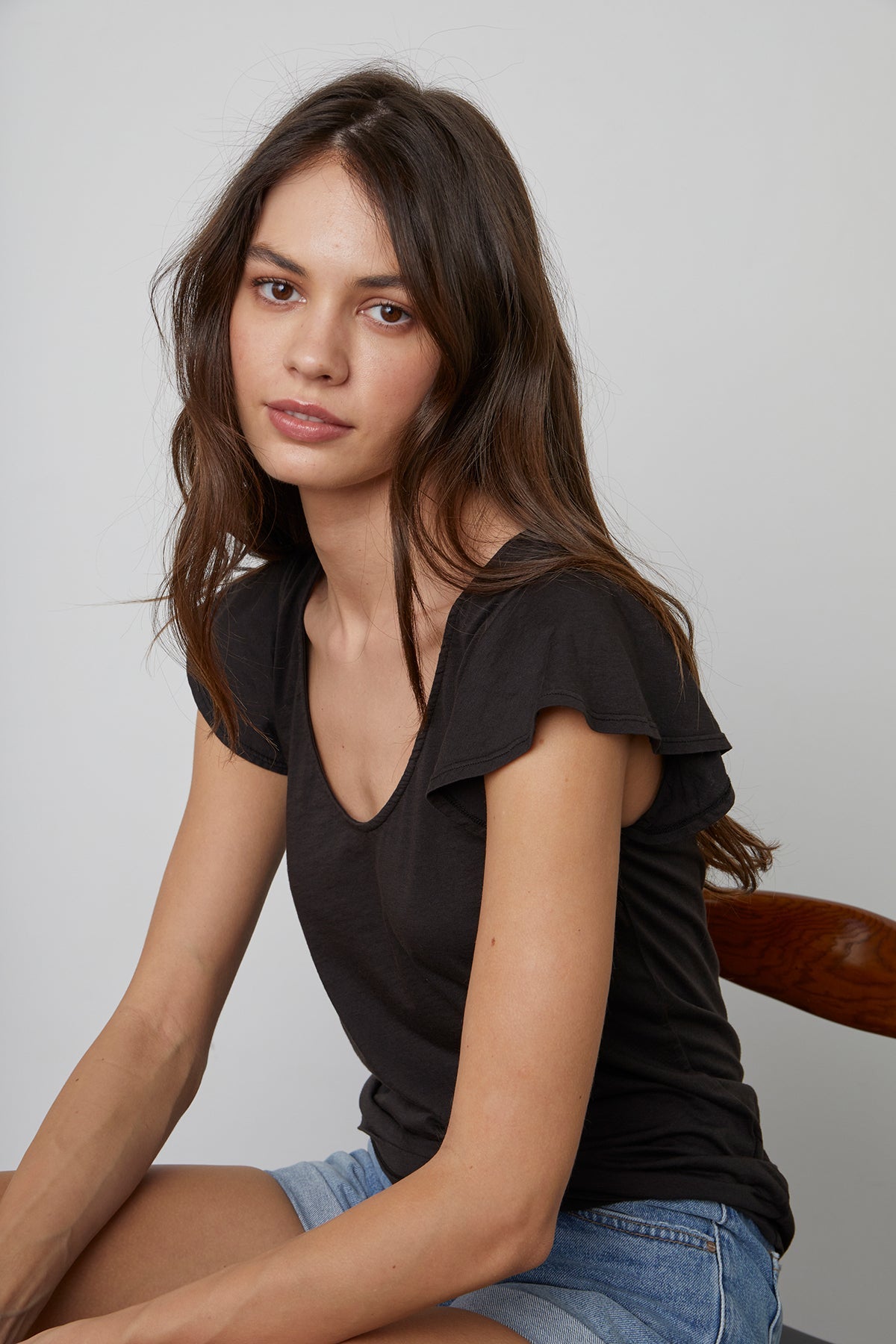 Rashida Scoop Neck Tee in Black with Natalie Denim Shorts in Seaside with Model Seated in Chair
