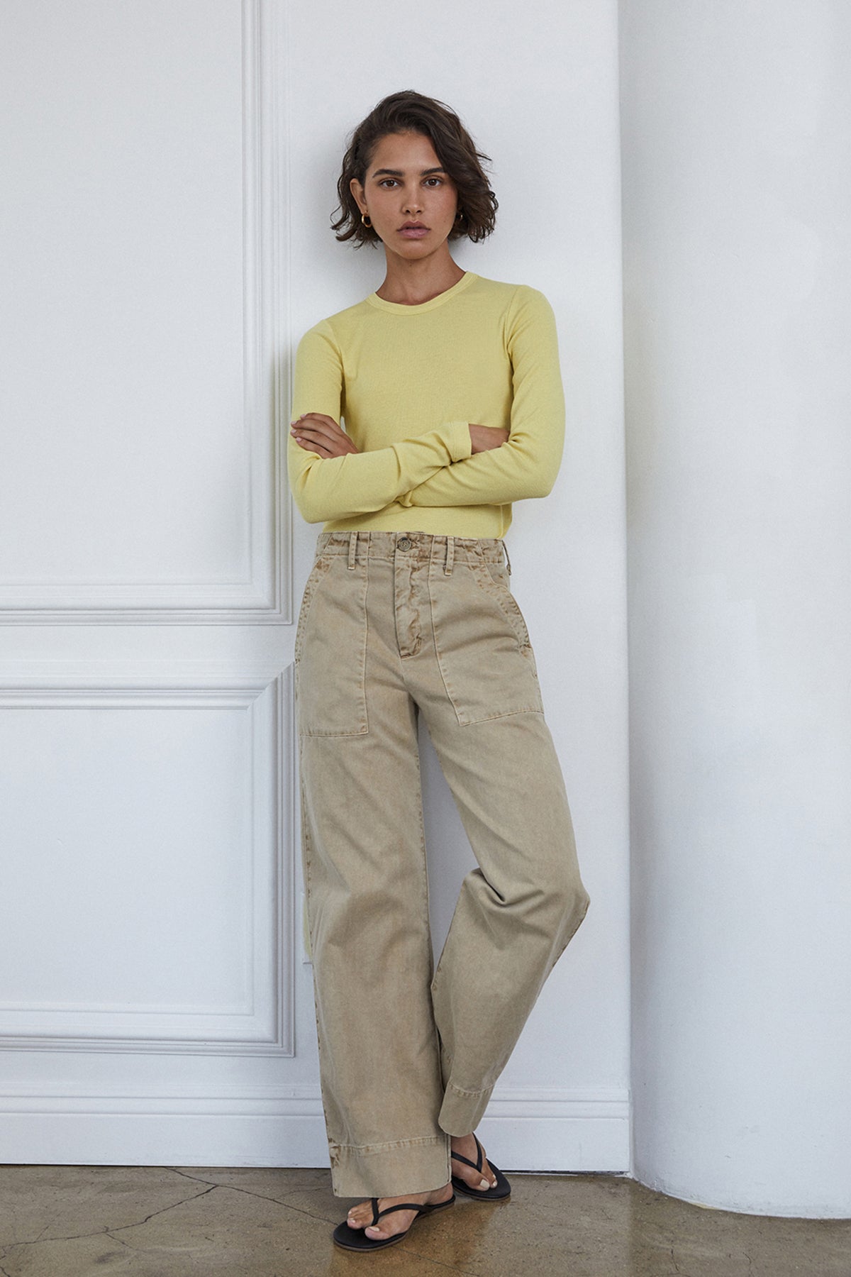   Model standing near wall with folded arms wearing Camino Tee in soft lemon yellow with Ventural pant in putty 