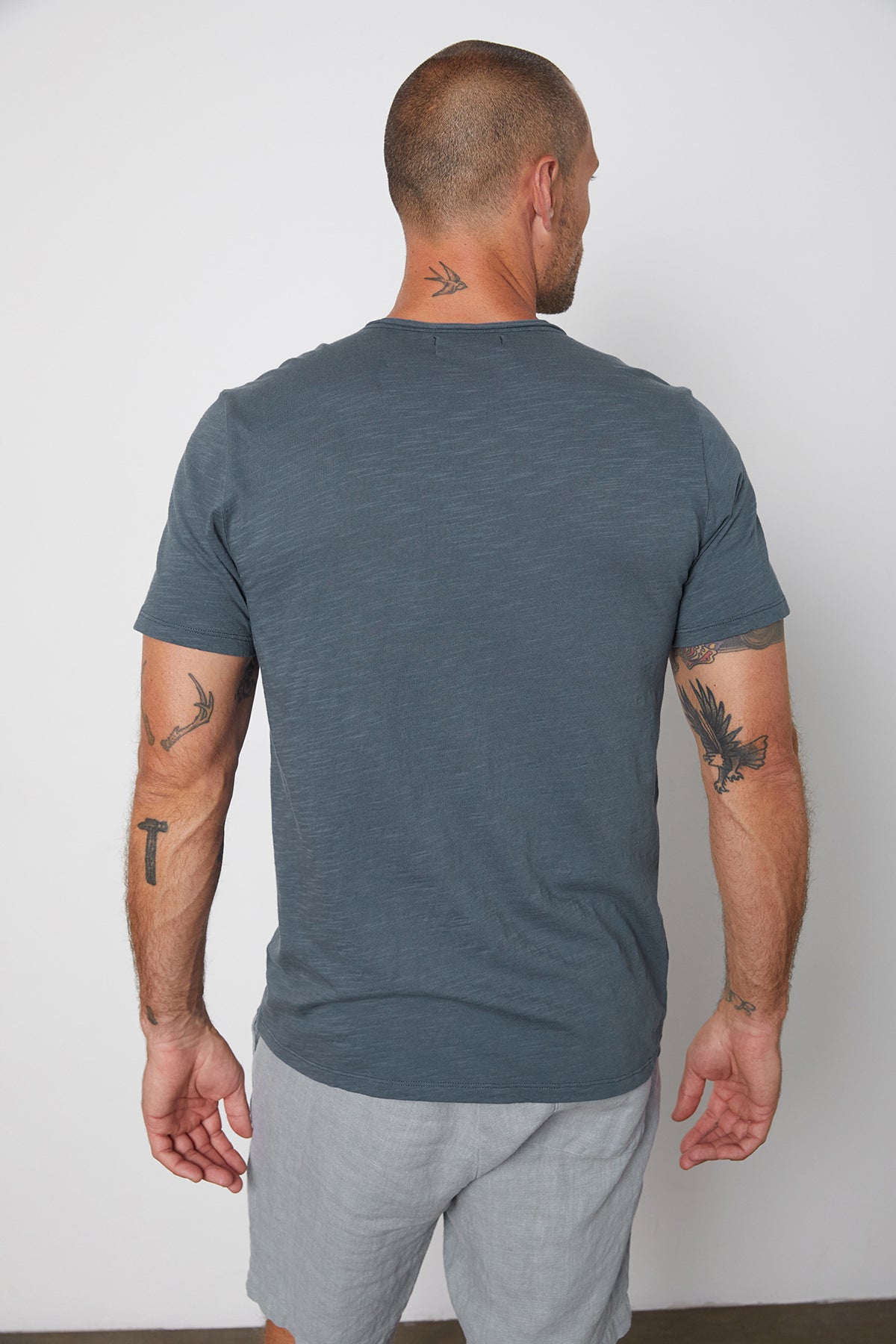   Back of Chad slub cotton tee with raw edges and front pocket in malachite, with Jonathan shorts in chambray. 